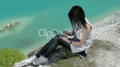 Young Woman Use A Tablet Sitting On A Hill Near Beautiful Lake