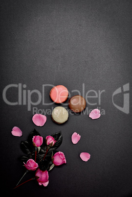 black background with macaroons and a bouquet of pink roses