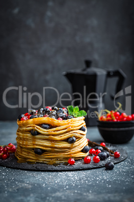 Pancakes with fresh berries and maple syrup on dark background, closeup