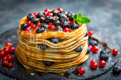 Pancakes with fresh berries and maple syrup on dark background, closeup