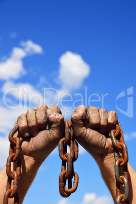 Two men's hands in the mud hold a rusty metal chain