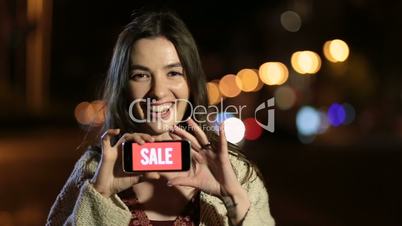 Girl holds phone with sale ad on screen at night