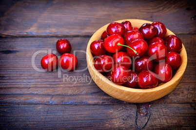Ripe red cherry in a wooden plate, top view