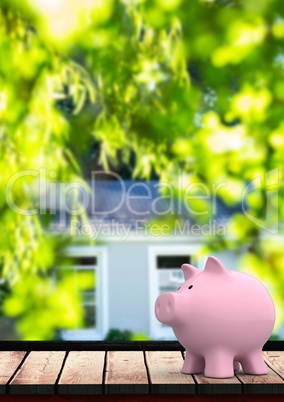 pink piggy bank against house with leafs(blurred)