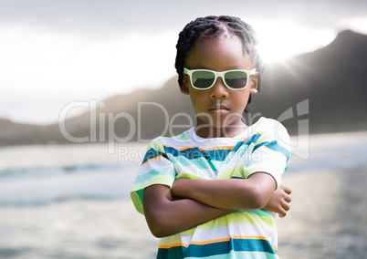Boy in sunglasses arms folded against coastline with flare