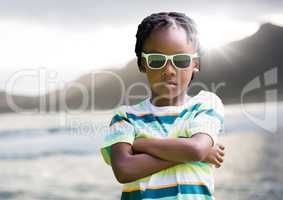 Boy in sunglasses arms folded against coastline with flare