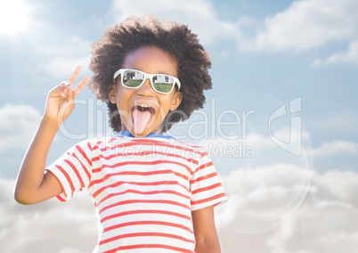 Boy in sunglasses making peace sign against sky with flare