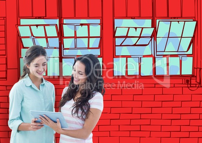 2 young women with tablet looking the new  office lines. Red wall of bricks with windows