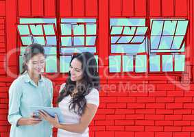 2 young women with tablet looking the new  office lines. Red wall of bricks with windows