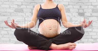 Pregnant woman mid section meditating against white brick wall