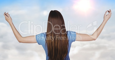 Back of woman with arms outstretched against sunny sky