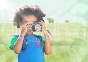 Boy with camera against meadow with flare