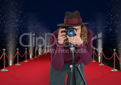 photographer with hat taking a photo with tripod  in the red carpet . Lights behimd
