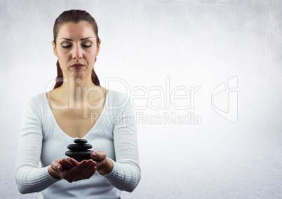 Woman meditating with stones against white wall