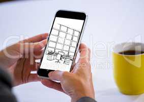 hands with phone with coffee behind. On the screen of the phone a blueprint of the design of the new