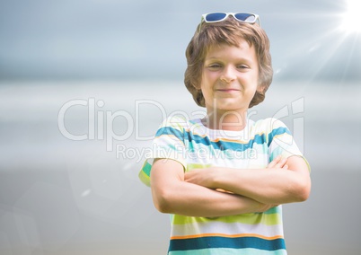 Boy in sunglasses arms folded against blurry beach with flare