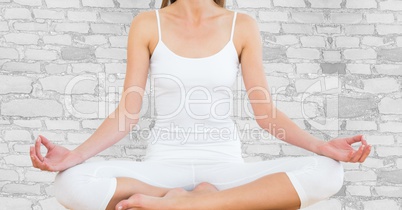 Woman mid section meditating against white brick wall