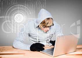 Blond-hair hacker using a laptop on wood table in front of grey background