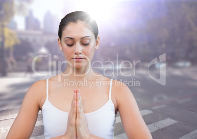 Woman meditating against blurry street with flare