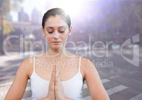 Woman meditating against blurry street with flare