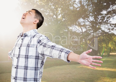 Man with arms outstretched against blurry park with flare