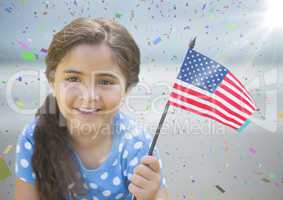 Girl with american flag against blurry beach with flare and confetti