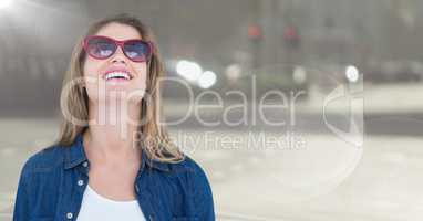 Woman in sunglasses smiling against blurry street with flare