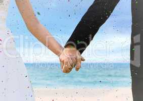 Confetti and bride and groom holding hands at blurry beach