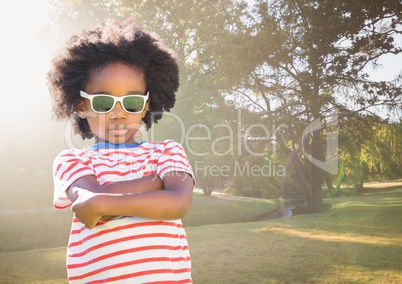 Boy in sunglasses arms folded against blurry park with flare