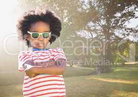 Boy in sunglasses arms folded against blurry park with flare