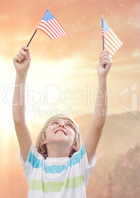 Smiling boy holding american flags against sunny landscape