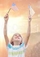 Smiling boy holding american flags against sunny landscape