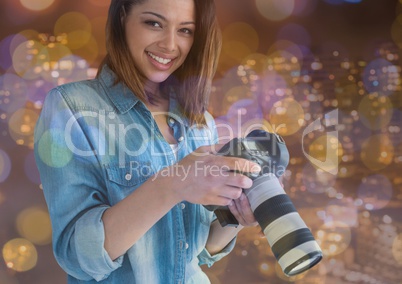 photographer woman smiling with camera on hands in the balcony. city nights lights and flares
