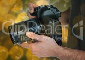 camera on photographer hands. Green and yellow bokeh background and overlap.