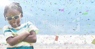 Boy in sunglasses arms folded against blurry beach with flare and confetti
