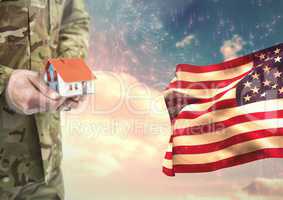 Soldier holding a little house close to the american flag