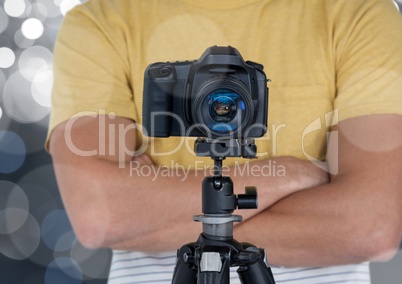 photographer hands folded with camera with tripod in front. Silver bokeh behind