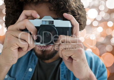 photographer smiling and taking a photo with vintage camera. Brown and white blurred lights behind