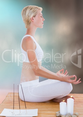 Woman meditating with candles against blurry blue brown background