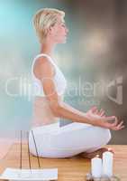 Woman meditating with candles against blurry blue brown background
