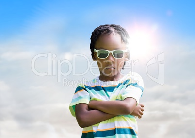 Boy in sunglasses arms folded against sky and sun with flare