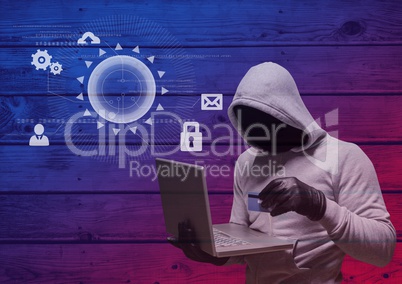Hacker with hood holding a credit card and using a laptop in frond of wood background with digital i