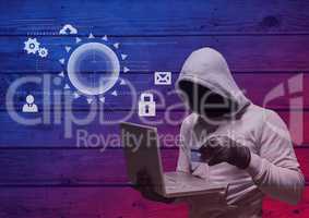 Hacker with hood holding a credit card and using a laptop in frond of wood background with digital i