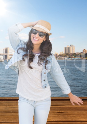 Woman with hand on summer hat against water and skyline with flare