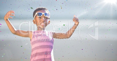 Boy in sunglasses hands out against blurry beach with flare and confetti