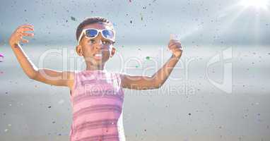 Boy in sunglasses hands out against blurry beach with flare and confetti