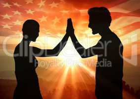 Silhouette of people high fiving against sunset and american flag