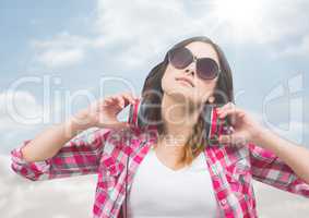 Woman with headphones against sunny sky with flare