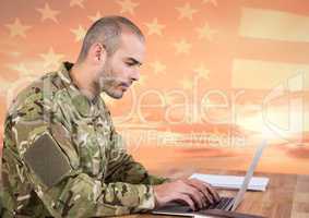 Soldier using a laptop in front of american flag