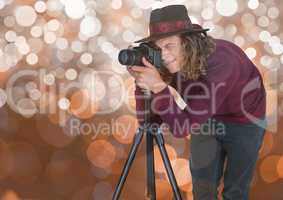 young hipster photographer with hat taking a photo with the tripod. Brown bokeh